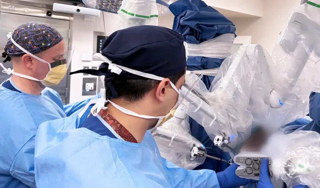 Surgeons operating robotic surgical equipment in theatre.