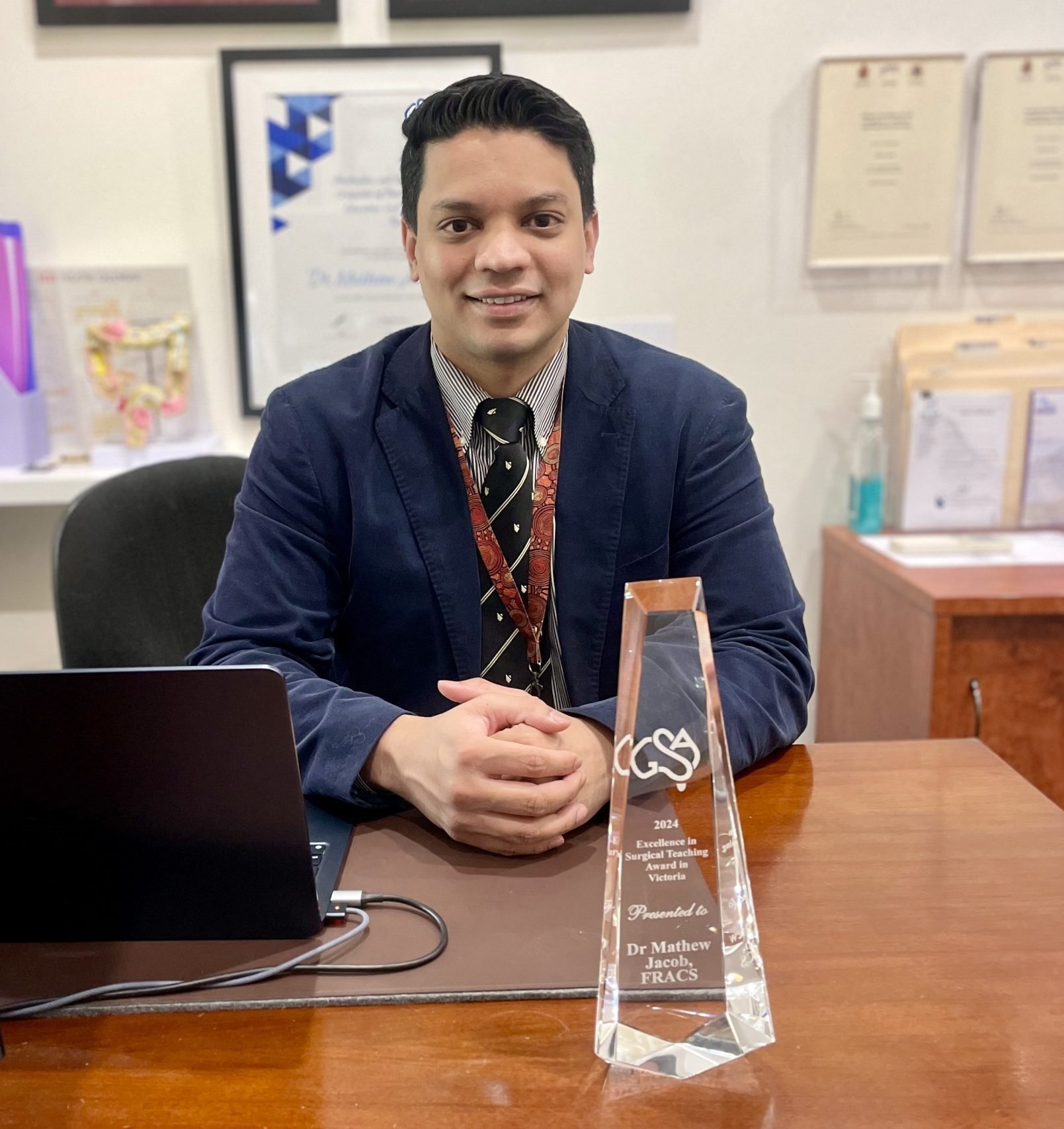 Man at desk with award and framed certificates.